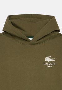 Φούτερ από βαμβάκι σε ελιά χρώμα με μπροστινή τσέπη τύπου καγκουρό, μεγάλο καπέλο και λευκό κεντητό λογότυπο Lacoste στο αριστερό στήθος.