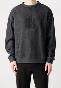 Sweat-shirt à rayures noires avec une texture côtelée, col rond, épaules tombantes et logo délavé sur le devant. Associé à un pantalon noir.