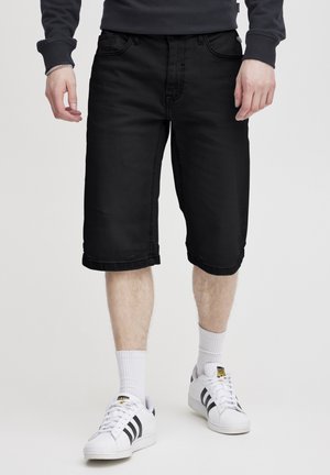 Črni denim kratke hlače s ravnim krojem, zavihki, petimi žepi, gladko teksturo in minimalističnim dizajnom. Uporabljene z belimi nogavicami in čevlji.