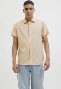 Korte mouw, geknoopte blouse van licht perzikkleurige stof, met een kraag en rechte zoom, gecombineerd met lichtblauwe jeans.