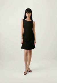 Vestido preto sem mangas com um design simples, silhueta reta e decote arredondado. Usado com sandálias pretas de tiras.