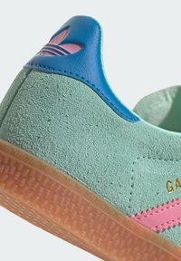 Baskets en daim vert avec une surface texturée, talon en cuir bleu, rayure rose et semelle en gomme transparente. Présente un détail de logo doré.