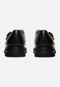 Schwarze Lederschuhe mit runder Spitze, subtiler Textur und einem Buckle-Akzent mit niedrigem Kontrast. Dicke Gummisohle für Langlebigkeit und Komfort.