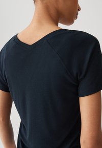 Schwarzes, geripptes Kurzarmoberteil mit V-Ausschnitt. Hat eine taillierte Silhouette und kontrastierende Textur an den Schultern und am Rücken.