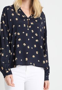 Marinblus med v-ringning, prydd med små blommönster i kräm och grönt, långa ärmar och en avslappnad passform.