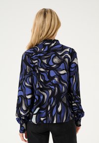 Langärmlige Bluse mit einem fließenden Design in Blau-, Schwarz- und Grautönen. Verfügt über eine gemusterte Textur und elastische Bündchen.