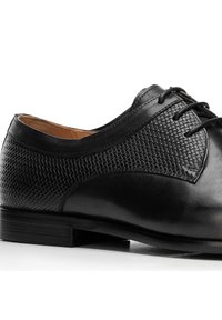 Černá kožená společenská bota s texturovaným tkaným panelem, kulatou špičkou a tkaničkami, s hladkým povrchem a nízkým podpatkem.