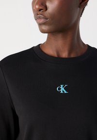 Schwarzer Sweatshirt mit rundem Ausschnitt und weicher Textur. Verfügt über ein hellblaues, gesticktes "cK"-Logo auf der Brust.