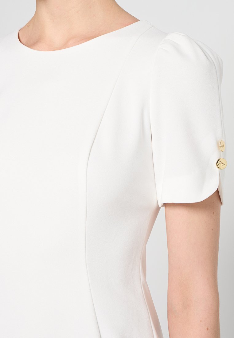 Biała sukienka z okrągłym dekoltem i krótkimi bufiastymi rękawami. Złote guziki w akcentach na rękawie. Gładki, płynący materiał o eleganckim kroju.