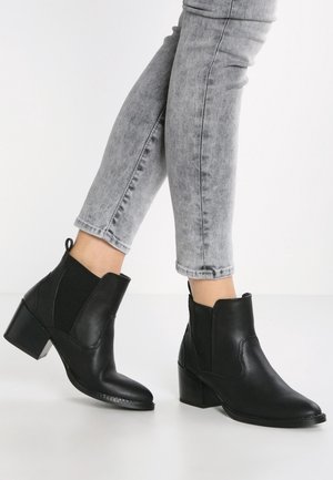 Stivali alla caviglia in pelle nera con pannelli laterali elasticizzati, punta affilata e tacco medio a blocco, abbinati a pantaloni in denim grigi.