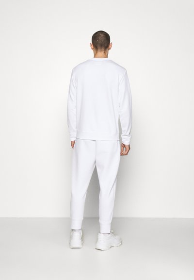 Sweatshirt blanc à manches longues et col rond, associé à un jogging assorti. Tissu doux et texturé, avec des poignets et une taille ajustée.