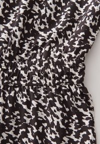 Tessuto a fantasia bianco e nero con un design maculato, dotato di una vita elasticizzata per una vestibilità comoda. Texture morbida con un drappeggio fluido.