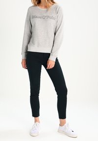 Sudadera gris con el logo "Marc O'Polo", cuello redondo y puños de canalé. Combinada con pantalones negros ajustados y zapatillas blancas.