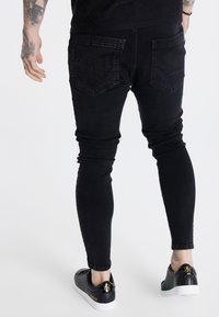 Jeans skinny negros con un diseño texturizado en el bolsillo trasero. Forma ajustada con un acabado suave, combinados con zapatos en blanco y negro.