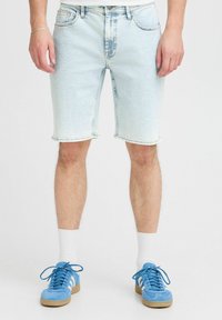 Ljusblå denimshorts med en urtvättad look, midjehöjd, och fransad fåll. Bärs med ljusblå sneakers och vita strumpor.