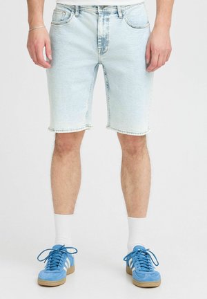Ljusblå denimshorts med en urtvättad look, midjehöjd, och fransad fåll. Bärs med ljusblå sneakers och vita strumpor.