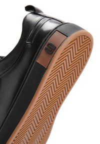 Czarny skórzany sneaker z brązową gumową podeszwą o zygzakowatym wzorze bieżnika i małym wytłoczonym logo przy pięcie.