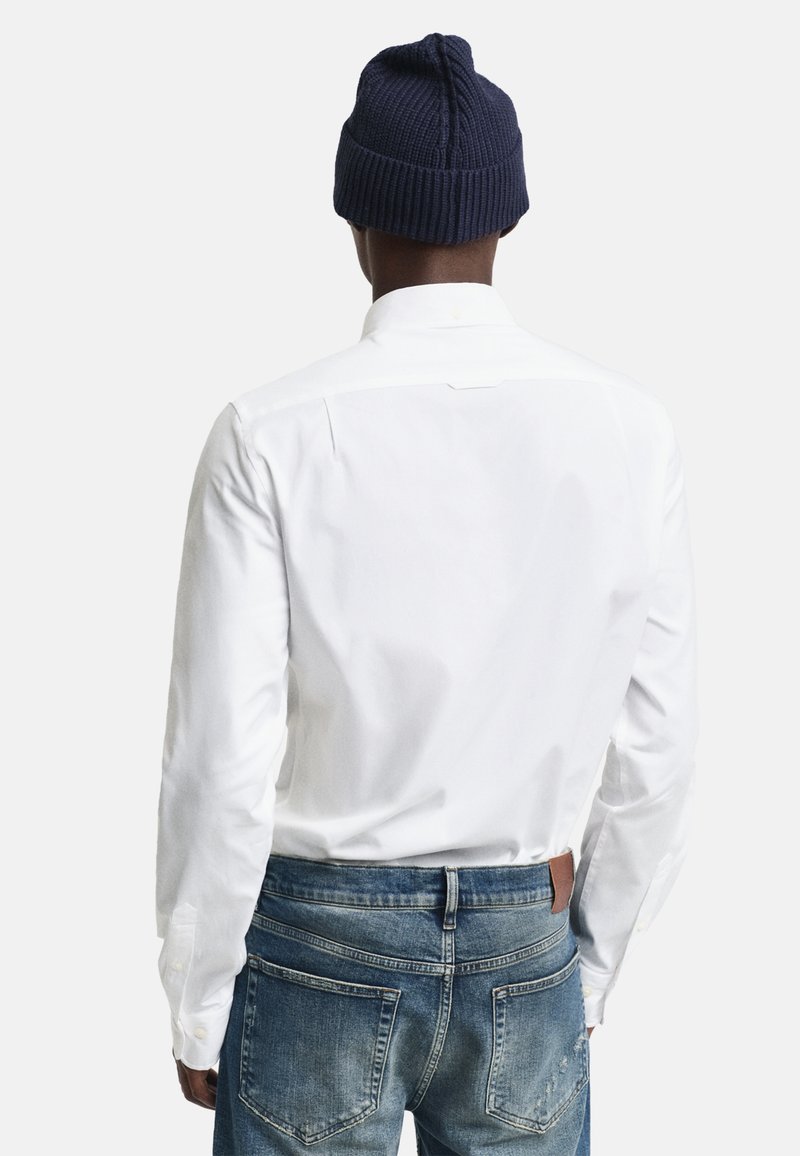 Chemise blanche à manches longues avec boutons, en coton lisse, détail au dos, associée à un jean en denim bleu clair et un bonnet en tricot marine.