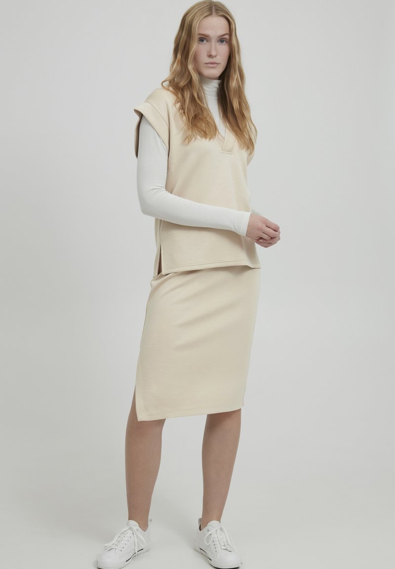 Crème-kleurige tweedelige outfit bestaande uit een top met korte mouwen en een rok tot de knie, gemaakt van zachte stof met een losse pasvorm.