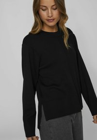 Pull en tricot noir avec des manches longues, un col rond, des fentes sur les côtés et un ourlet droit. Texture lisse avec une coupe décontractée.