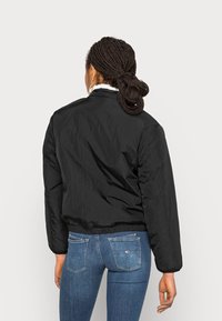 Czarna bomberka o gładkiej, lekkiej fakturze oraz elastycznych mankietach. Posiada miękki, biały kołnierz. Noszona z niebieskimi dżinsami.