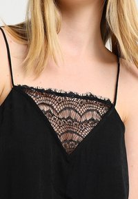 Svart linne med tunna remmar, med en spetskrage med scallopade kanter och intrikata vågmönster. Lättviktig tyg; enkel design.