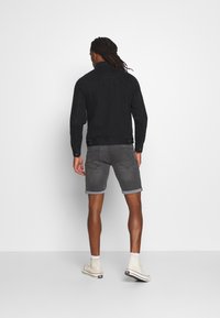 Chaqueta de mezclilla negra, pantalones cortos grises enrollados y zapatillas de caña alta beige. El conjunto presenta un ajuste casual y elementos de diseño simples.