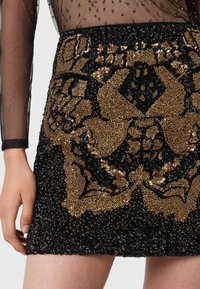 Czarna spódnica mini z cekinami w złotym kolorze, ozdobiona skomplikowanymi wzorami z koralików, o fakturowanej powierzchni i dopasowanym kroju z końcem tuż nad udem.