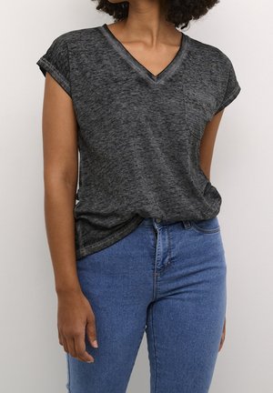 Person wearing a dark gray V-neck short sleeve top with a chest pocket and blue high-waisted jeans against a plain background.