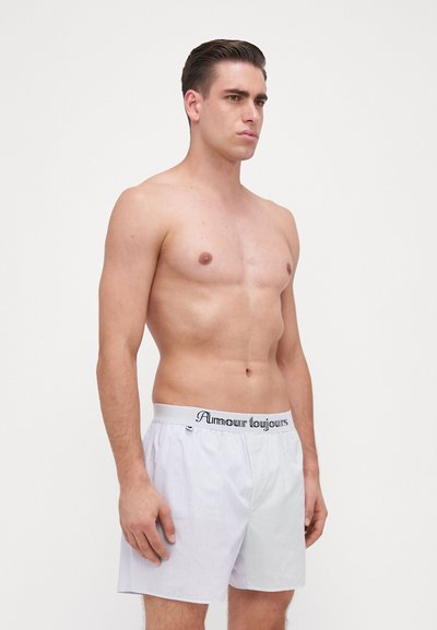 White and light blue striped cotton boxer shorts with a black logoed waistband, featuring a relaxed fit and clean hemline.