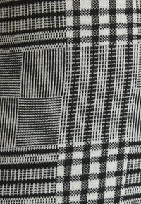 Black and white knitted fabric featuring a checkered and striped pattern with various textures, including smooth and ribbed sections.