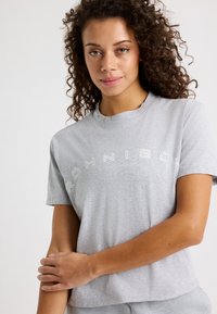 Camiseta de algodón gris con cuello redondo, manga corta y texto de logo impreso en blanco. Textura suave, corte holgado y diseño casual.