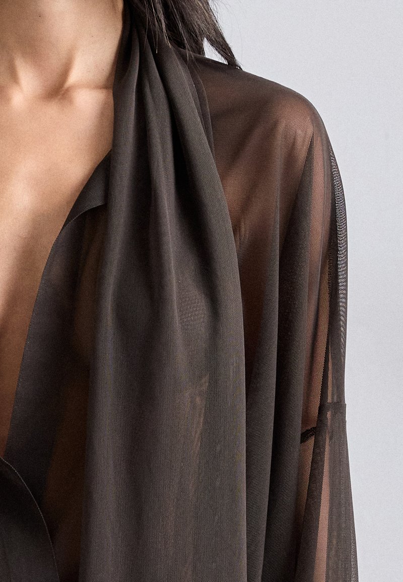 Kimono nero trasparente con una morbida texture, tessuto leggero e davanti allungato, caratterizzato da un design drappeggiato e maniche aperte.