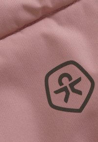 Gaiši rozā audums ar gludu tekstūru, kas rotāts ar tumšu sešstūra logo dizainu un apmalēm.