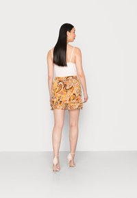 Top branca de alças com bordado de renda, combinado com uma saia mini de padrão paisley colorido com camadas franzidas; modelo usa sapatos de salto nude.
