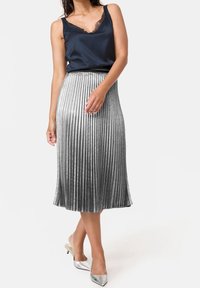 Top de satén azul marino con detalles de encaje, combinado con una falda midi plisada plateada. La falda presenta líneas verticales y un dobladillo acampanado. Tacones plateados de punta.