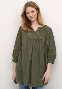 Olivgrön blus med V-ringning, broderade detaljer och ballongärmar. Tillverkad av lätt tyg, med en rynkad kroppsstil.