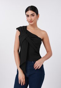Μαύρο τοπ με έναν ώμο και λεπτομέρεια με στριφτό κόμπο στη λαιμόκοψη. Απαλό ύφασμα με ομαλή υφή. Συνδυάζεται με σκούρο μπλε τζιν.