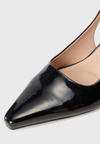 Escarpin noir en cuir verni à bout pointu avec un design épuré, des côtés ouverts et une doublure intérieure lisse. Présente un talon fin et une finition brillante.