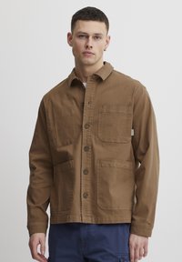 Veste en coton marron avec un bouton à l'avant, deux poches poitrine et une coupe décontractée. Elle présente un col et des manches longues.