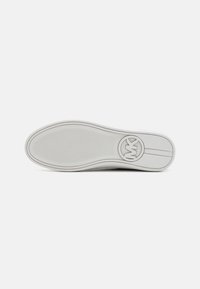 Semelle de chaussure gris clair avec grip texturé, logo rond près du talon et détail à double bande sur la zone lisse du talon.