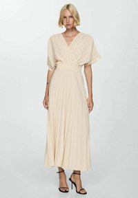 Rochie plisată bej cu design înfășurat și mâneci scurte, având o talie ajustată și fustă fluidă. Purtați cu sandale negre cu curea.