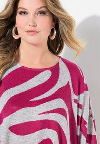 Maglione grigio con audaci motivi a onda rosa e bianci, dal taglio rilassato e con scollatura rotonda. Orecchini a cerchio argentati completano il look.