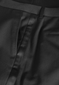 Melna auduma ar gludu satīna apdari, ar plakanām šuvēm, diskretu kabatu un vidukļa joslu. Tekstūra ir gluda un viendabīga.