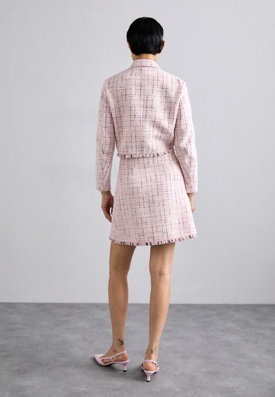 Rosa tweed to-delt drakt med en kort jakke med frynser og et matchende miniskjørt. Stoffet har en teksturert vev med flerfargede tråder.