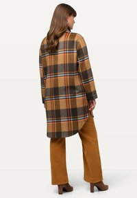Rutigt skjortjacka i bruna, orange och blå nyanser. Tillverkad av textil med struktur, långa ärmar och rundad nederkant. Matchad med orange manchesterbyxor.