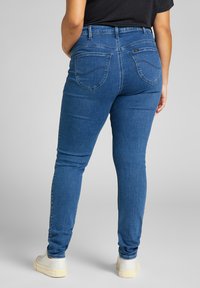 Niebieskie skinny jeansy z wysokim stanem, z klasycznym pięciopocketowym wzorem i subtelnymi detalami szycia. Połączone z białymi trampkami.