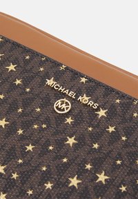 Borsa in tessuto marrone scuro con motivo a stelle dorate, logo "Michael Kors" dorato e inserti in pelle beige nella parte superiore.