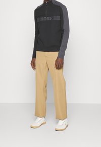 Ciemnoszary sweter z kołnierzykiem na zamek błyskawiczny, z czarnym logo "BOSS" na piersi. Połączony z beżowymi spodniami i białymi trampkami.