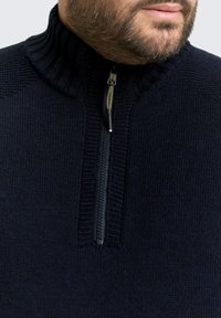 Marineblauwe trui met ritssluiting en een hoge geribbelde kraag, voorzien van een gestructureerd breipatroon en een contrasterende ritssluiting met gouden accenten.